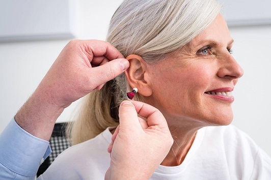 Ältere Frau bekommt ein modernes Hörgerät angepasst, Hörgeräteakustiker Beratung.